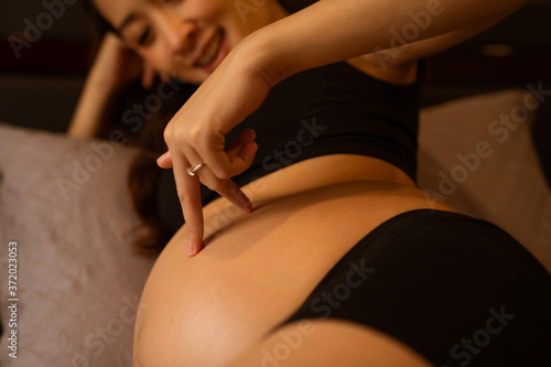 Close-up hand of a pregnant woman touching her belly on the foreground in emotional smile happy by asian woman