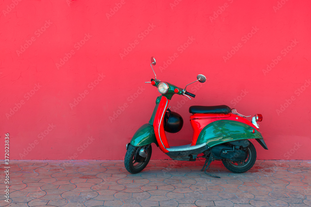 Electric red green scooter parking against the background of a solid pink wall on a city street. Car sharing concept