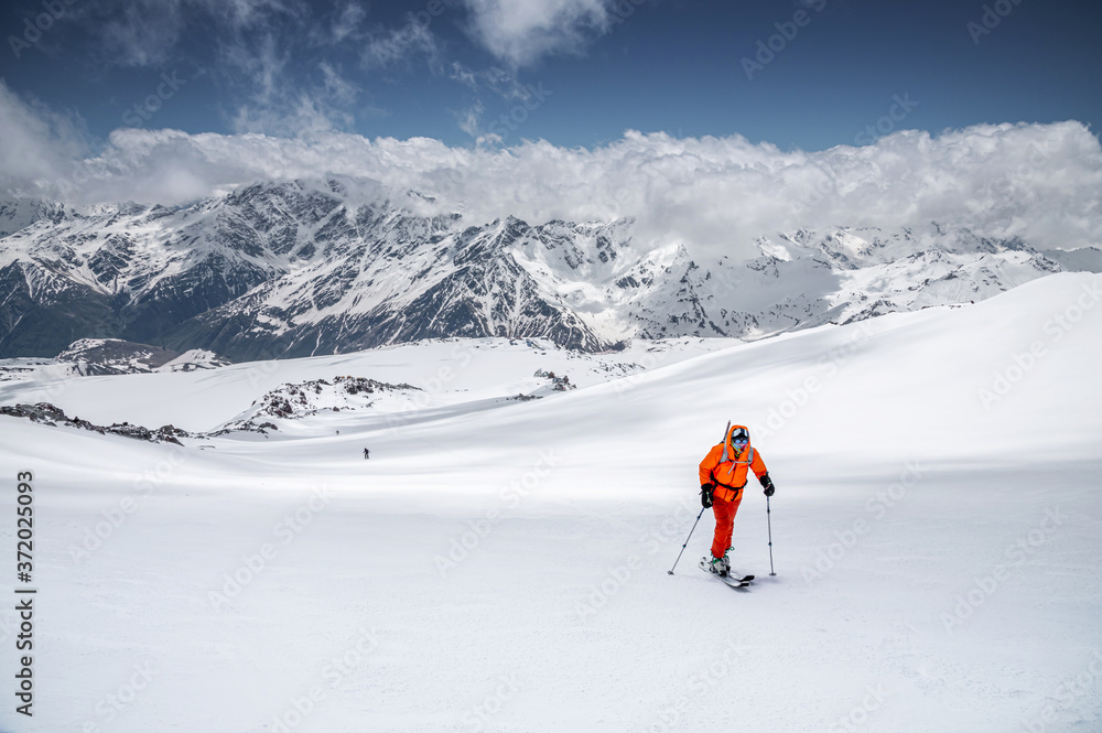 A skier in an orange suit skis in a mountain off-piste skiing in the northern caucasus of Mount Elbrus