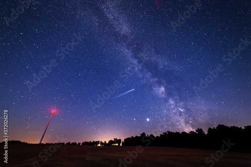 Milky Way Galaxy over a windmill field with falling star across.