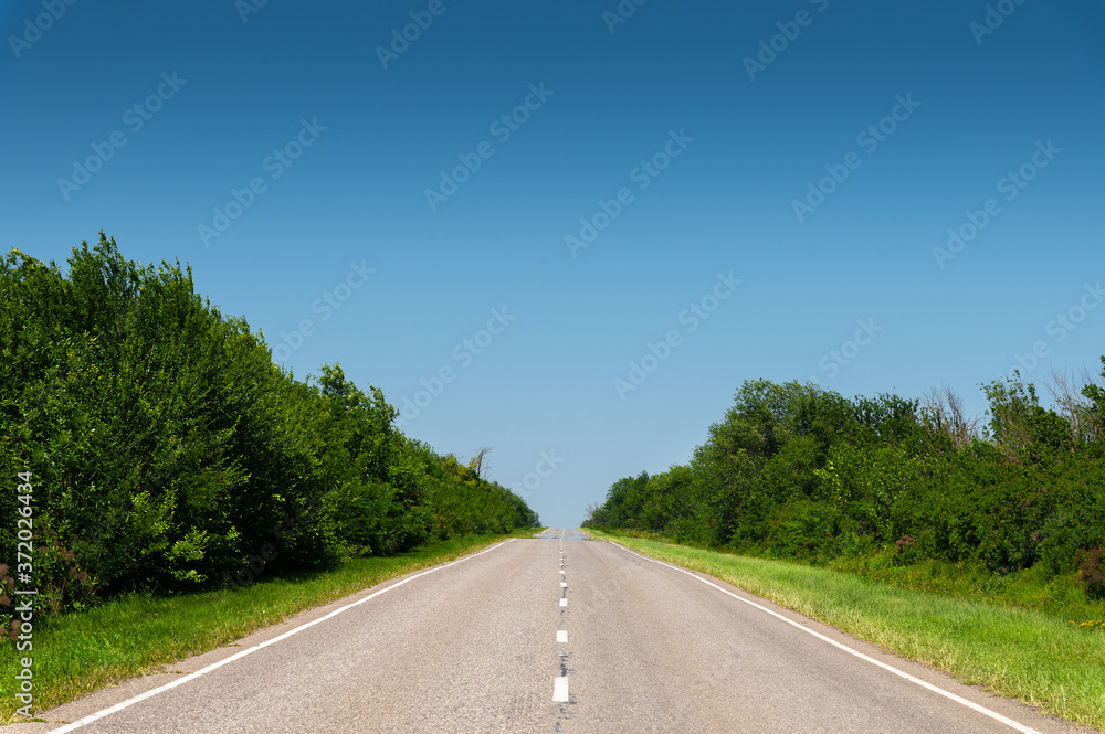 suburban empty road asphalt surrounded by trees and grass. The concept of transportation and travel. Background green grass asphalt and blue sky suburban empty road asphalt surrounded by trees and grass. The concept of transportation and travel. Background green grass asphalt and blue sky