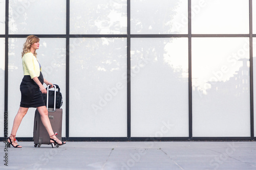 A pregnant woman passing by a modern building with travel luggage