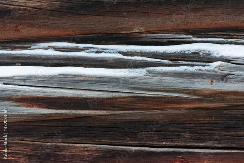 Abstract texture with detail of old wooden wall from logs under snow