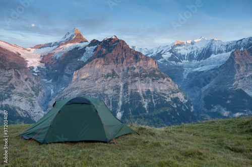 Green tent in the mountains during a colorful sunset. Night bivouac, million star hotel under night sky, tent on pass in Alps. Camping in the high mountains.
