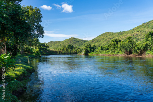 Fototapeta Naklejka Na Ścianę i Meble -  The clear stream flowing in the river reflects the blue sky. Flows through the mountains at the Kwai Yai River, Kanchanaburi, Thailand.