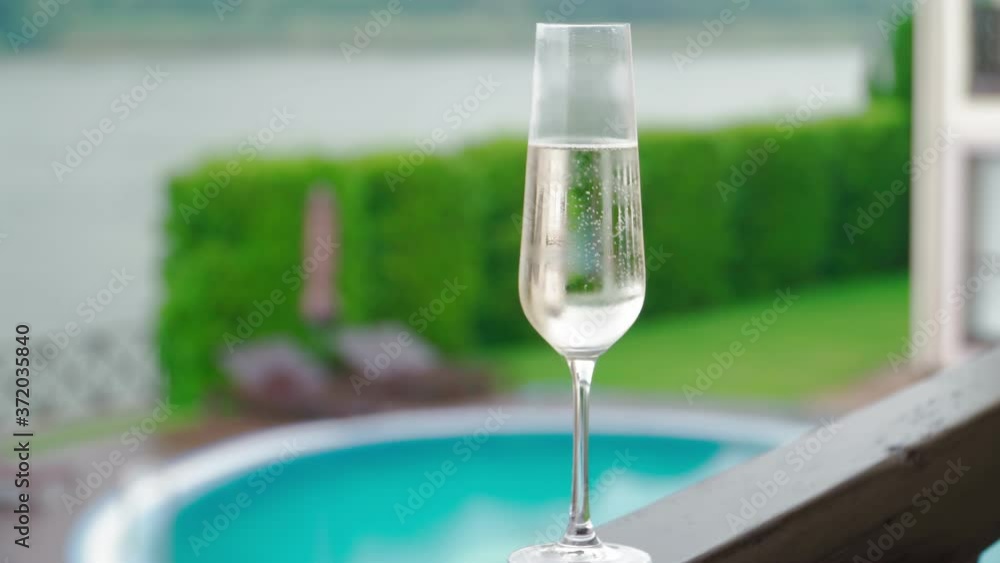 White champagne or prosecco glass against poolside at luxury resort hotel during vacation Close-up. Refreshing alcohol drink. Slow motion White champagne or prosecco glass against poolside at luxury resort hotel during vacation Close-up. Refreshing alcohol drink. Slow motion