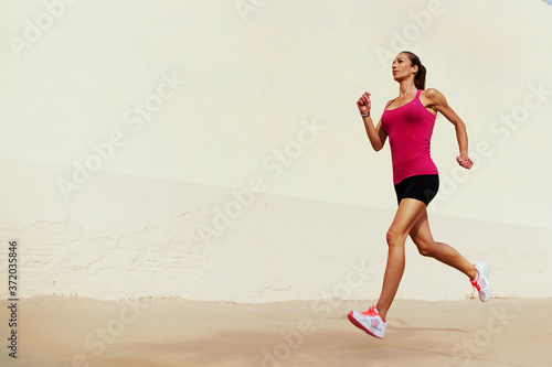 Full length portrait of female runner on morning jog against with copy space area wall for your text message or information, healthy sports woman with sexy figure playing sports outdoors in summer day