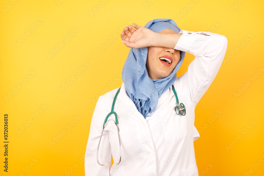Φωτογραφία young beautiful Arab doctor woman wearing medical uniform standing over yellow background covering eyes with arm smiling cheerful and funny