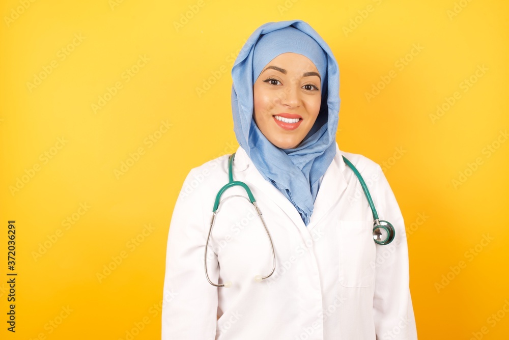 Young arab doctor woman wearing medical uniform standing over yellow background with a happy and cool smile on face. Lucky person. Young arab doctor woman wearing medical uniform standing over yellow background with a happy and cool smile on face. Lucky person.