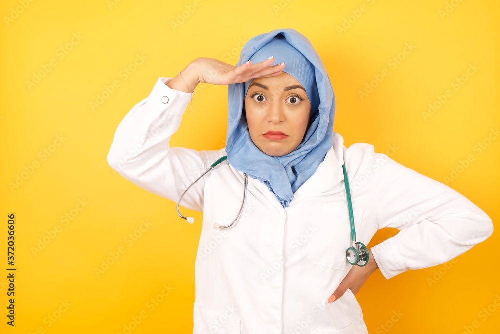 Φωτογραφία Young arab doctor woman wearing medical uniform standing over yellow background , having problems, worried and stressed holds hand on forehead