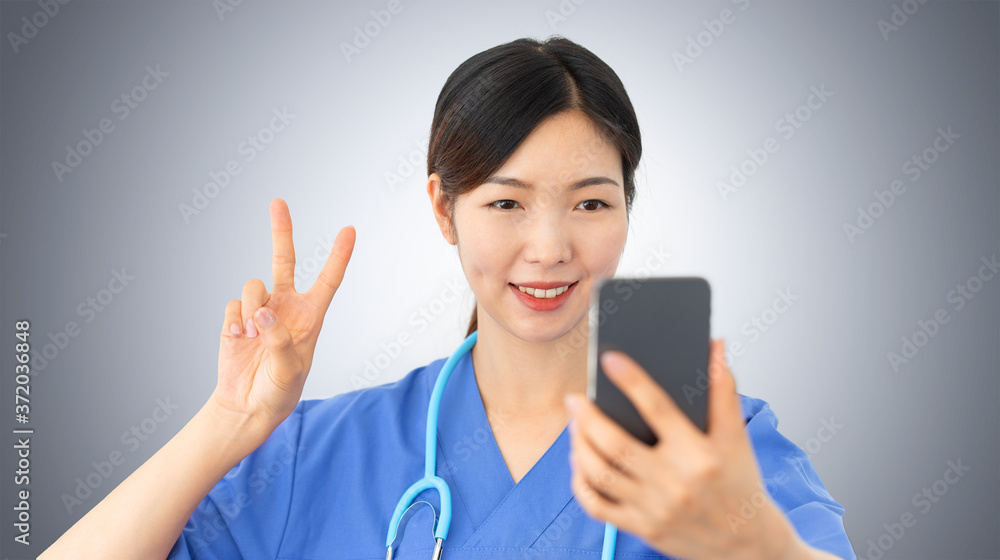 beautiful asian female doctor takes a selfie gesturing the victory sign with her fingers, confident health care professional makes a positive sign while holds a mobile beautiful asian female doctor takes a selfie gesturing the victory sign with her fingers, confident health care professional makes a positive sign while holds a mobile
