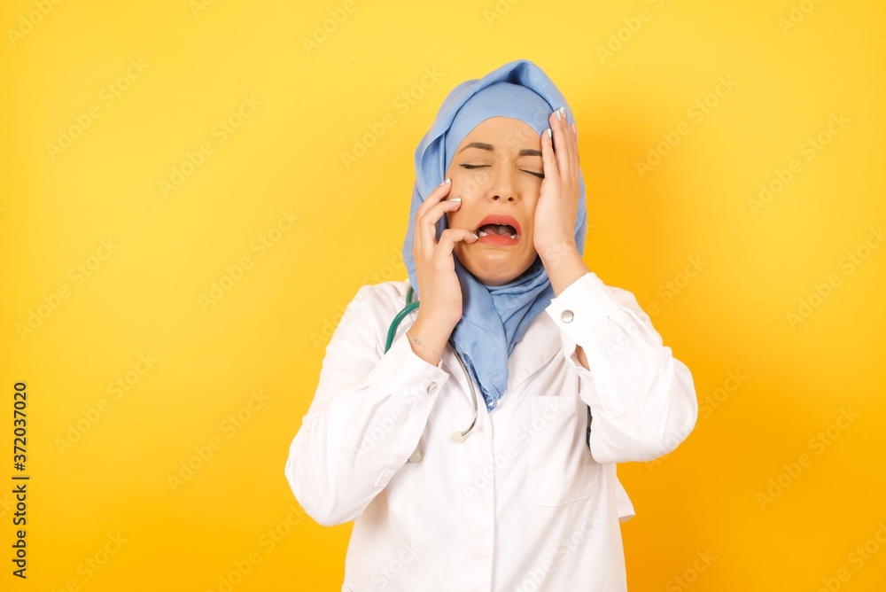 Doleful desperate crying Young arab doctor woman wearing medical uniform standing , being in depression after quarrel with someone, looks stressfully, frowns face. Pretty male feels lonely and anxious Doleful desperate crying Young arab doctor woman wearing medical uniform standing , being in depression after quarrel with someone, looks stressfully, frowns face. Pretty male feels lonely and anxious