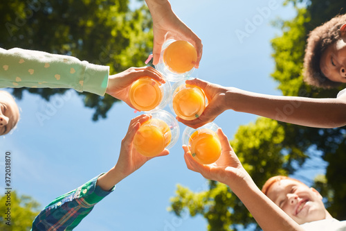 Low angle close up of kids holding glasses with orange juice against blue sky outdoors, copy space photo