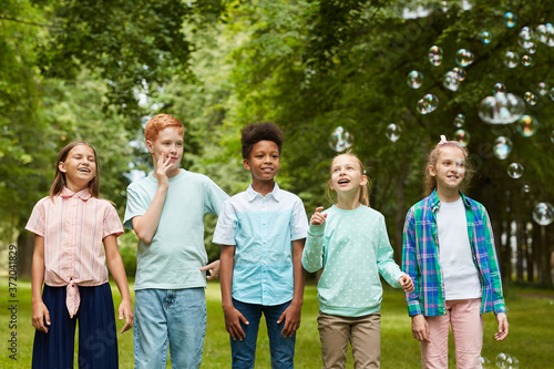 Front view portrait of multi-ethnic group of kids standing in row outdoors while playing with bubbles in park