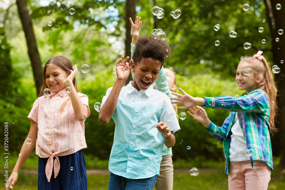 Waist up portrait of multi-ethnic group of carefree children playing with bubbles outdoors in park Waist up portrait of multi-ethnic group of carefree children playing with bubbles outdoors in park