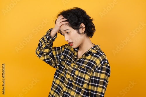A very upset and lonely Young beautiful Asian woman wearing plaid shirt over yellow background crying,  © Roquillo