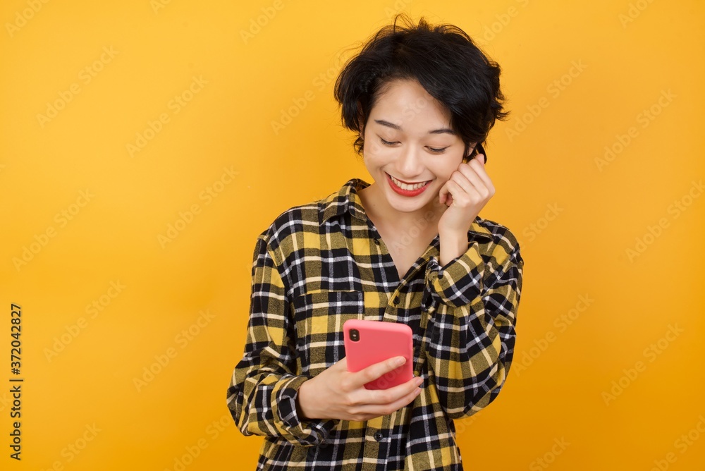 Joyous Young beautiful Asian woman wearing plaid shirt poses with mobile phone device, types text message on modern smartphone, watches funny video during free time, enjoys good internet connection, Joyous Young beautiful Asian woman wearing plaid shirt poses with mobile phone device, types text message on modern smartphone, watches funny video during free time, enjoys good internet connection,