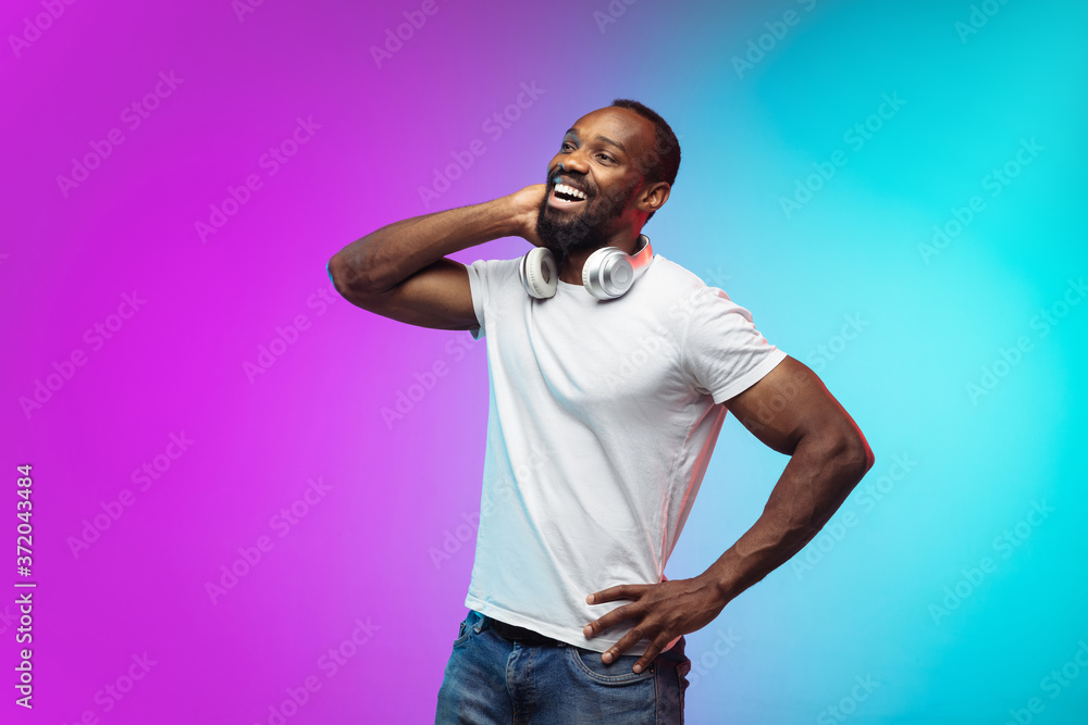 Laughting. African-american young man's portrait on gradient studio background in neon. Beautiful male model in casual style, white shirt. Concept of human emotions, facial expression, sales, ad. Laughting. African-american young man's portrait on gradient studio background in neon. Beautiful male model in casual style, white shirt. Concept of human emotions, facial expression, sales, ad.