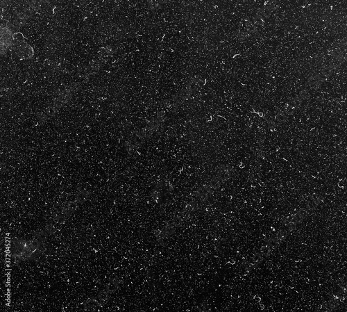 Photo of dust particles on a black monitor screen in the sun light. Chaotic white dots isolated on black background, abstract light spots texture.