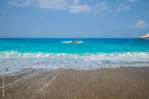 Fototapeta Naklejka Na Ścianę i Meble -  Foam covering the pebbles after big wave crushed on the beach with stunning turquoise water at Lefkada in Greece