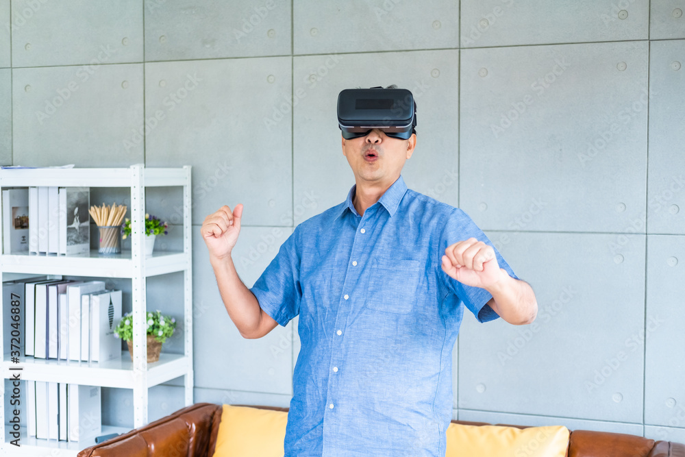 Senior Asian men feeling excited while wearing Virtual reality VR glasses inside of modern decoration house. New simulator technology and entertainment with Adult concept. Senior Asian men feeling excited while wearing Virtual reality VR glasses inside of modern decoration house. New simulator technology and entertainment with Adult concept.