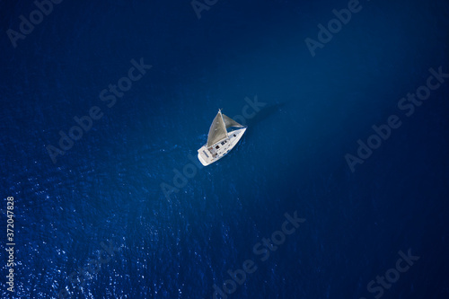 White sailboat in the rays of the sun on blue water top view