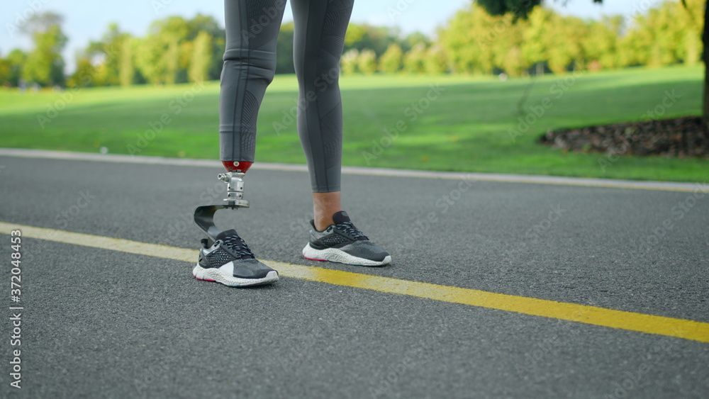 Woman with prosthetic leg standing on road.Athlete legs preparing to run in park