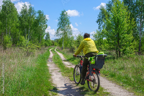 Dad in bright clothes rides his little daughter in a bicycle seat on a bicycle along a dirt road through the woods