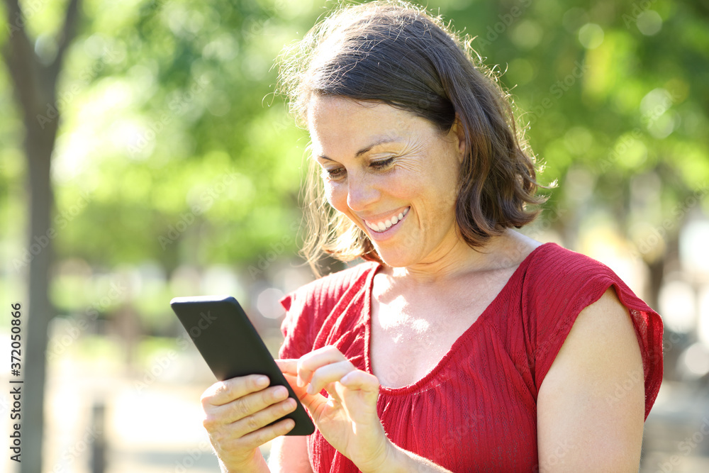 Happy adult woman texting on phone standing in the park Happy adult woman texting on phone standing in the park