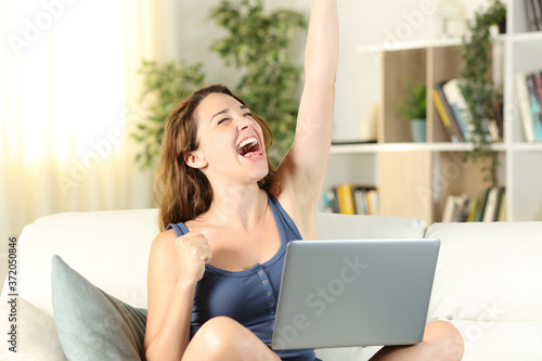Excited woman celebrates news on laptop on a couch at home