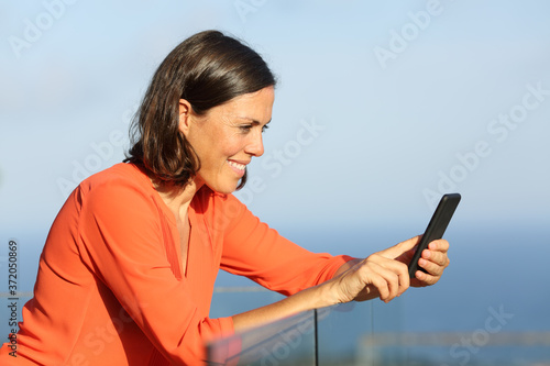 Happy adult woman using smartphone in a balcony