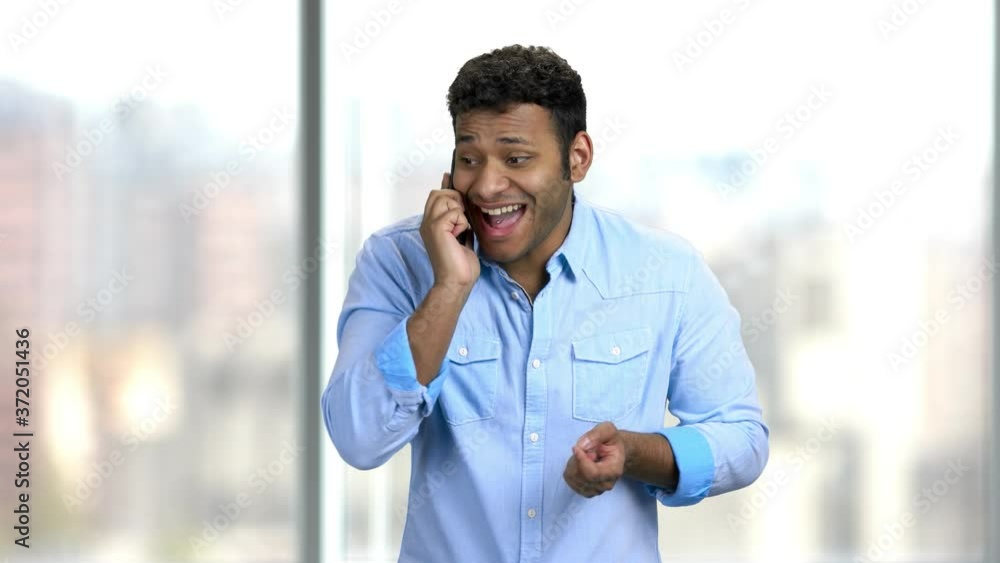 Happy businessman talking on cell phone. Young man celebrating success with hand. Blurred window background. Happy businessman talking on cell phone. Young man celebrating success with hand. Blurred window background.