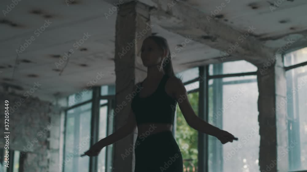 Cropped Slow Motion Shot of Female Athlete in Black Sportswear Jumping Rope. Woman Doing Jump Rope Fitness Cardio Workout in Dark Loft Industrial Building. Cropped Slow Motion Shot of Female Athlete in Black Sportswear Jumping Rope. Woman Doing Jump Rope Fitness Cardio Workout in Dark Loft Industrial Building.