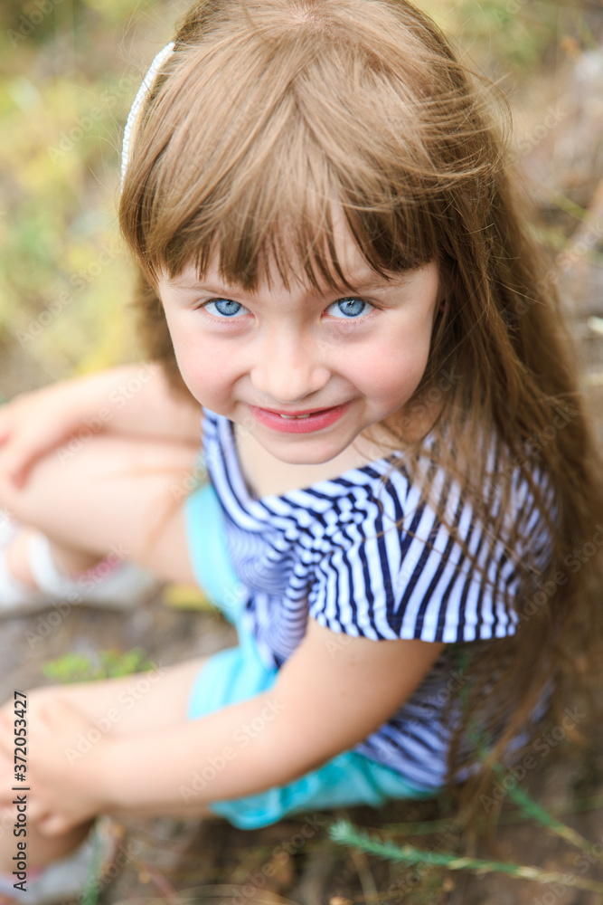 Portrait of a little blue-eyed girl. The girl is sitting on a stone. Portrait of a little blue-eyed girl. The girl is sitting on a stone.
