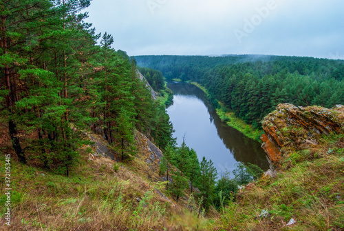 Beautiful river landscape with forest slopes of mountains. Limestone rocks in the Ural mountains. Cloudy sky in the background.