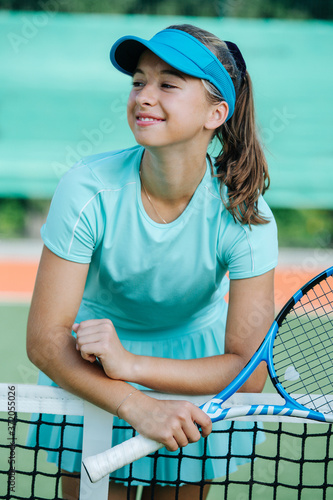 Happy smiling teenage girl standing on tennis court, leaning on the net, resting © zzzdim