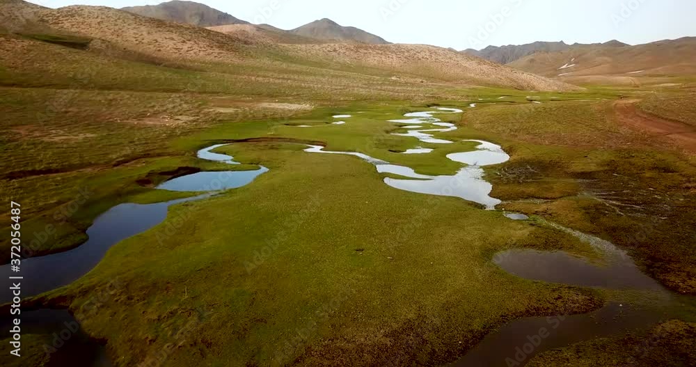 Hike in the middle of green meadow with calm pond stream reflects the sky in mountain highlands in spring a man wear a yellow Gore-Tex rain jacket walking by river Hike in the middle of green meadow with calm pond stream reflects the sky in mountain highlands in spring a man wear a yellow Gore-Tex rain jacket walking by river