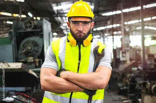 Portrait of industrial engineer worker wearing helmet and safely glasses standing with arms crossed, holding wrench and working at manufacturing plant factory, young man working in industry