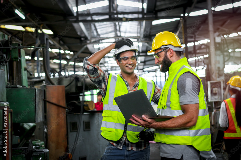 Industrial engineer wearing helmet and safe glasses, holding laptop computer for operating machinery at manufacturing plant factory, worker team working together in industry concept Industrial engineer wearing helmet and safe glasses, holding laptop computer for operating machinery at manufacturing plant factory, worker team working together in industry concept