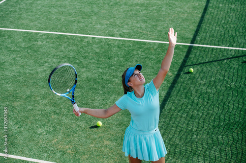 Squinting young girl training on a tennis court, throwing ball up and serving © zzzdim