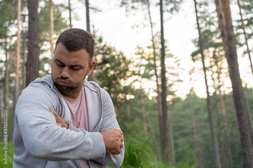 Pretty young beard man having pain in his biceps. Sitting in forest,surrounded with trees and beautiful nature. Pretty young beard man having pain in his biceps. Sitting in forest,surrounded with trees and beautiful nature.