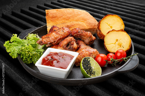 Grilled chicken wings with baked potatoes, matnakash and red sauce. Served in a cast iron pan photo