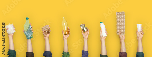 Partial view of group of people holding various types of garbage on yellow background