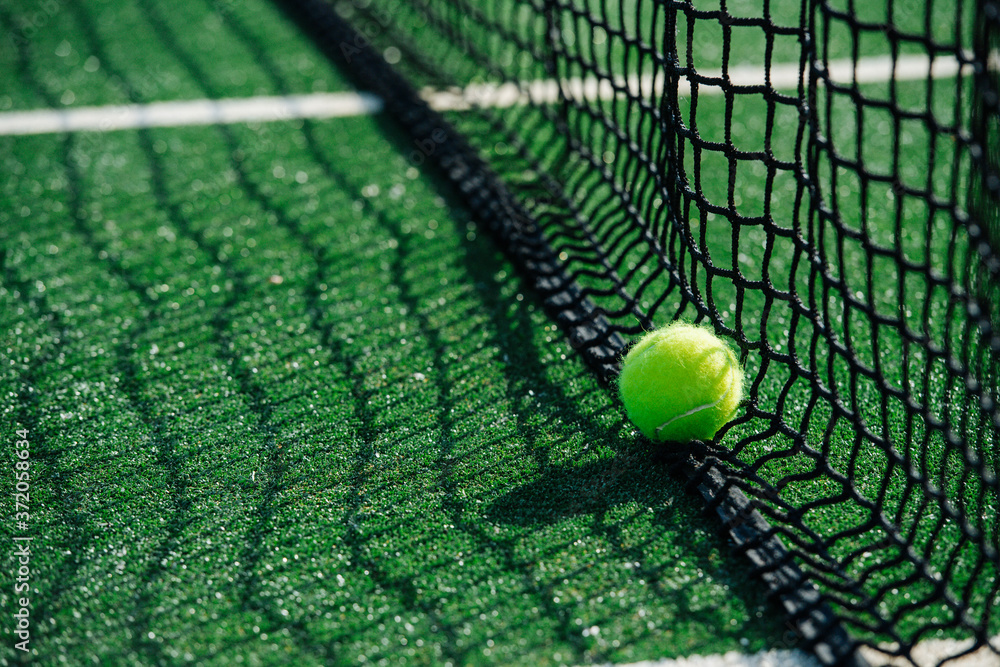 Yellow ball lying on the lower part of the net on a green tennis court