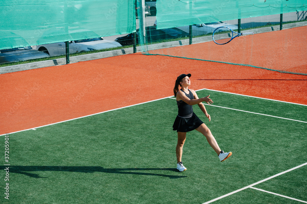 Carefree girl training on a tennis court, playing with racket, throwing it up