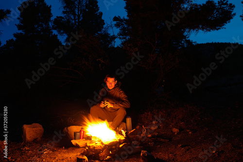 A young man sits by a campfire