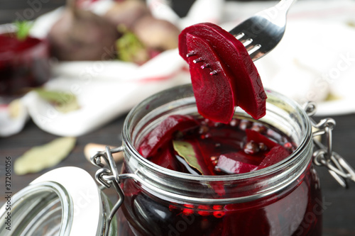 Fork with pickled beets over glass jar on wooden table, closeup