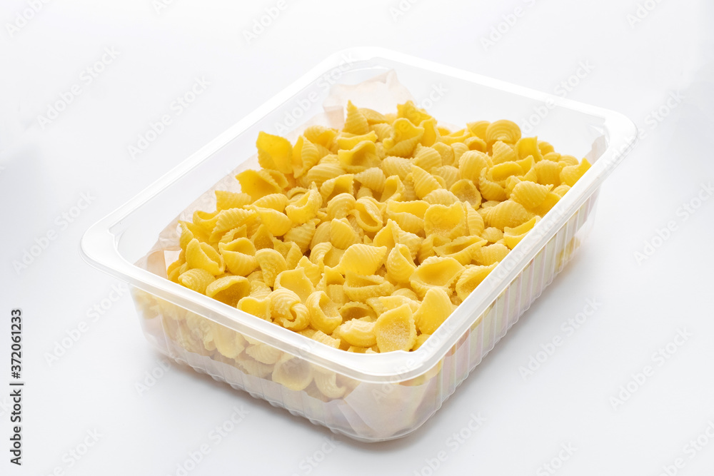 Raw conchiglie rigate macaroni in a plastic box isolated on a white background Raw conchiglie rigate macaroni in a plastic box isolated on a white background