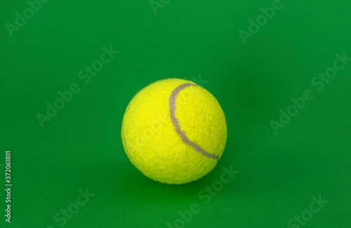 A single yellow tennis ball on a green background © mauro53