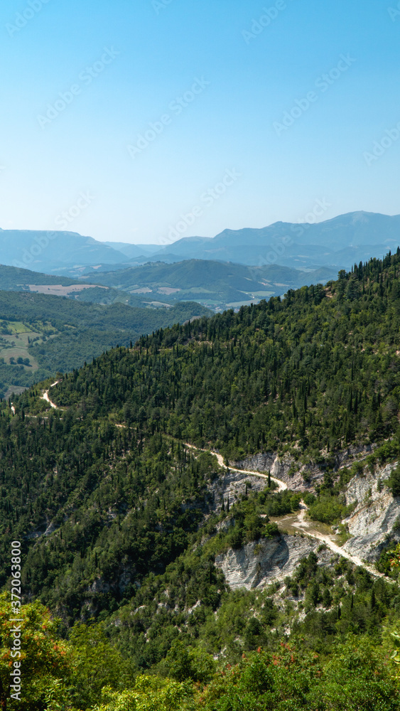 Paesaggio della Gola del Furlo con colline montagne verdi e stradina di ghiaia 